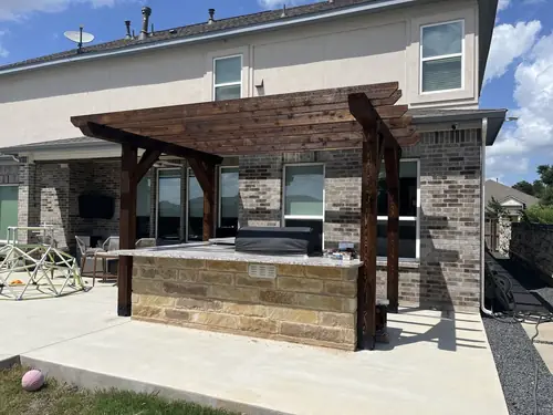 Stained cedar pergola shading a stone bar and grill station on a poured concrete patio