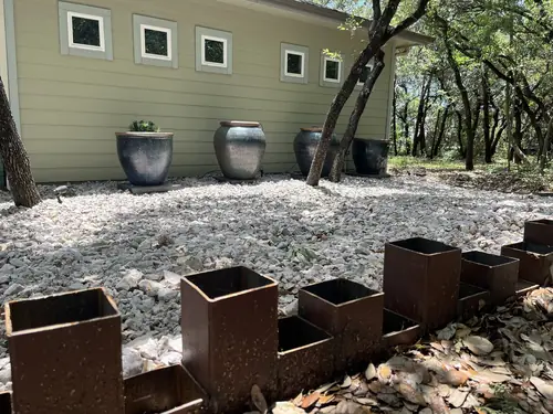 Crushed-stone bed with steel edging and glazed pots set against a Hill Country home