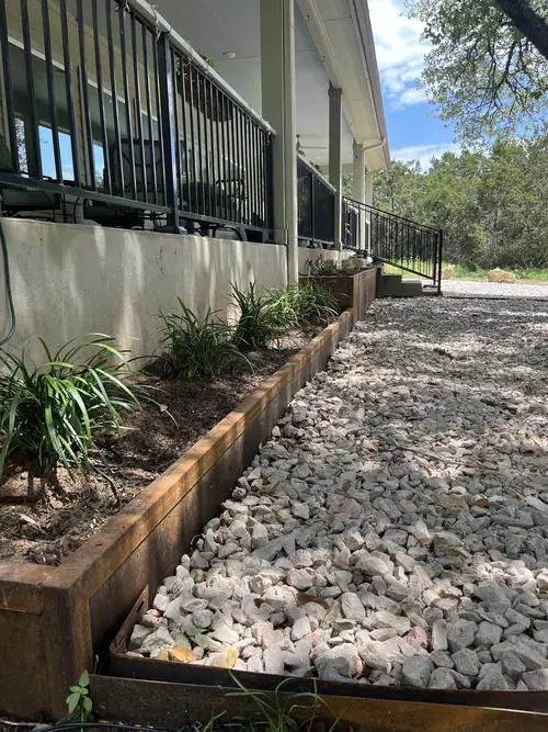 Long steel-edged planting bed and crushed-stone walk running the length of a covered porch