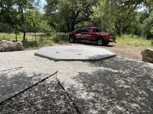 Octagonal composite deck pad set into a decomposed-granite clearing, with the company truck behind