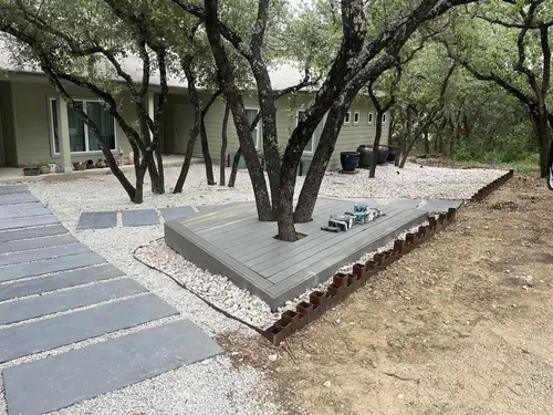 Tree-surround composite deck with a bluestone path and steel bed edging under mature oaks