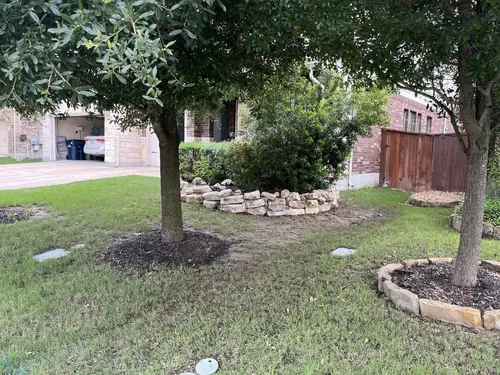 Dry-stacked limestone border wall and mulched tree rings in a front yard