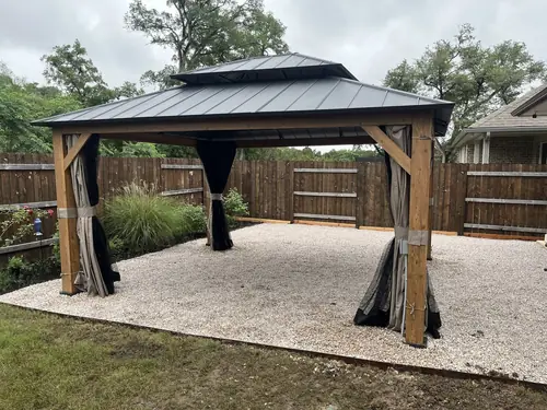 Hard-top gazebo set on a fresh gravel pad in a fenced back yard
