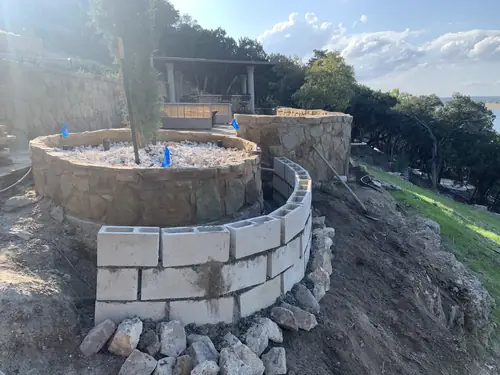 Curved stone-faced planter and block retaining wall under construction on a lakeside slope