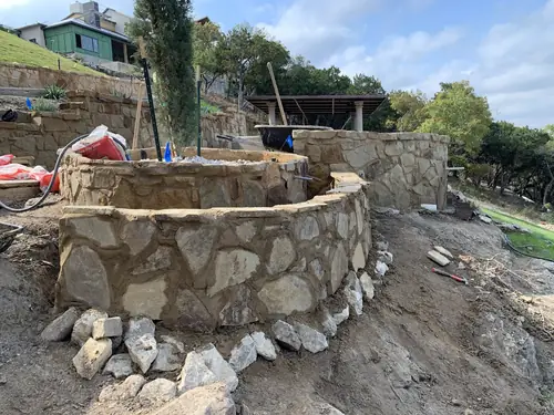 Hand-laid natural stone facing on a circular planter and retaining wall