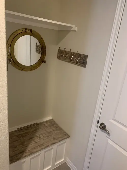 Mudroom nook with a built-in bench, porthole mirror and coat hooks seen from the doorway